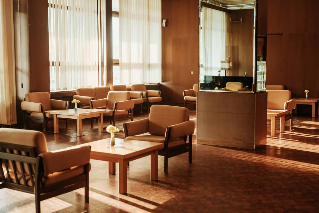 A warm lounge with armchairs, a low table and sunlight through tall curtains