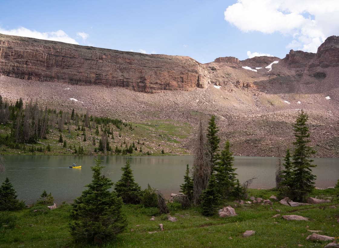 An alpine lake with conifers along the shore and a broad rocky ridge rising behind it