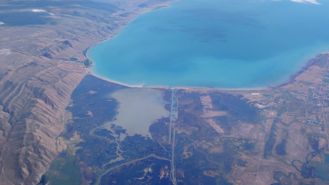 An aerial view of the turquoise water of Bear Lake on the Idaho-Utah line, with farmland and brown hills around its shore
