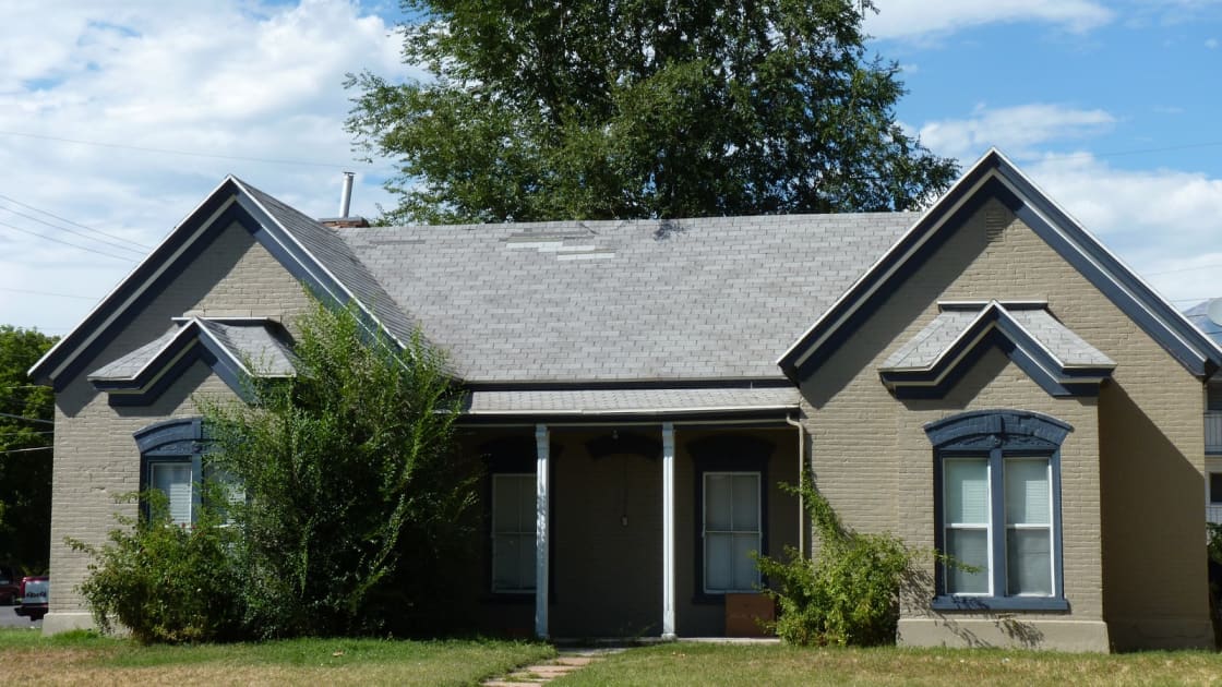 A single-story house with two front gables, dark trim and a covered porch, on a green lawn under a partly cloudy sky