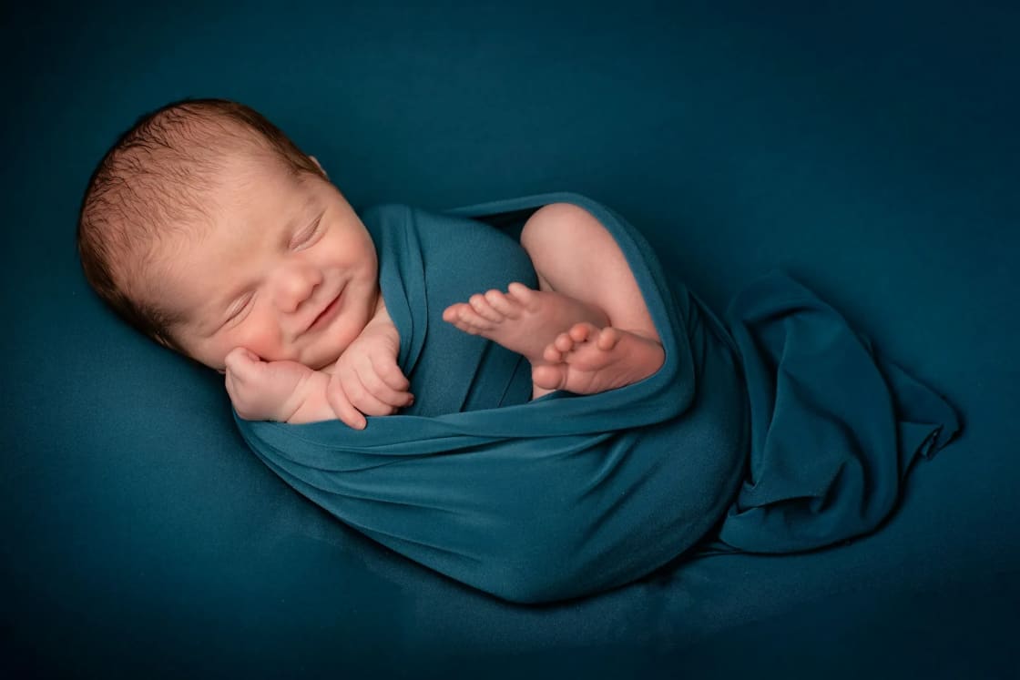 A sleeping newborn wrapped in a teal swaddle and posed on a matching teal backdrop, the classic studio newborn portrait.