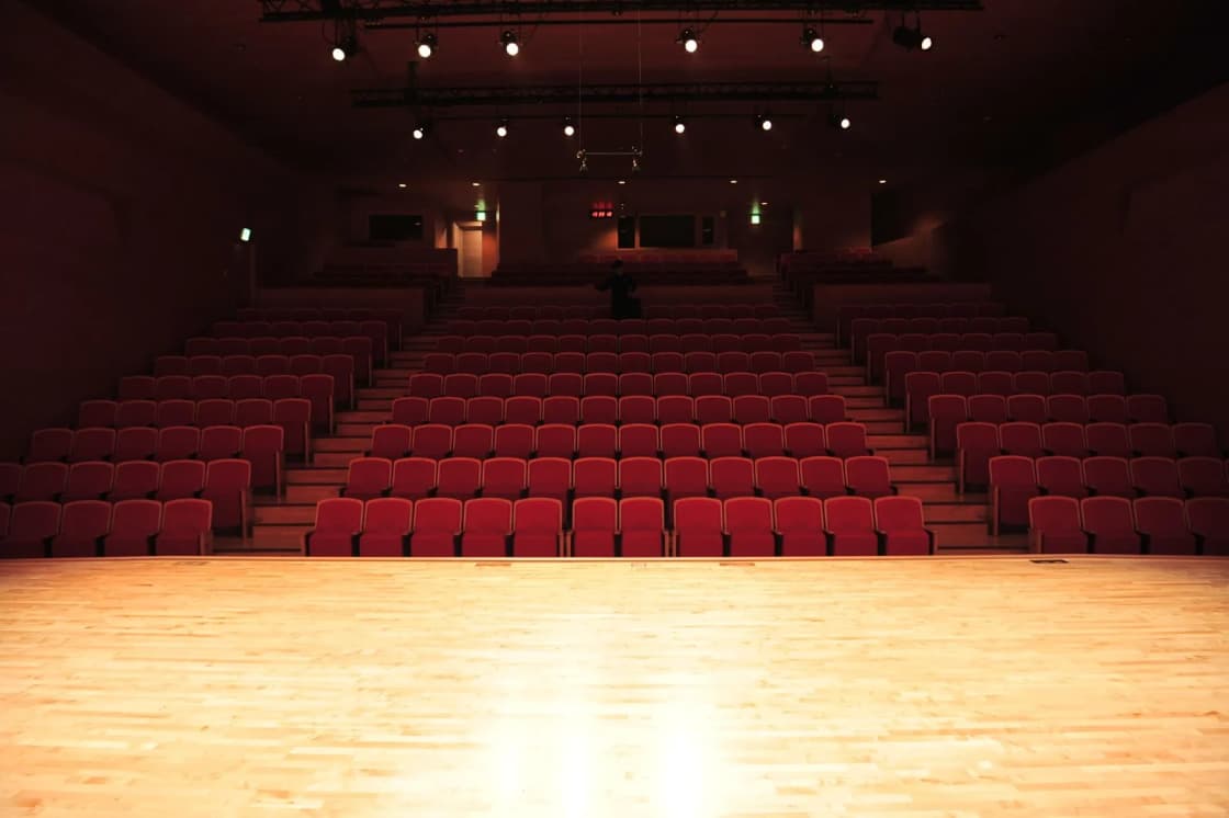 View from a lit wooden stage out over rows of red theater seats