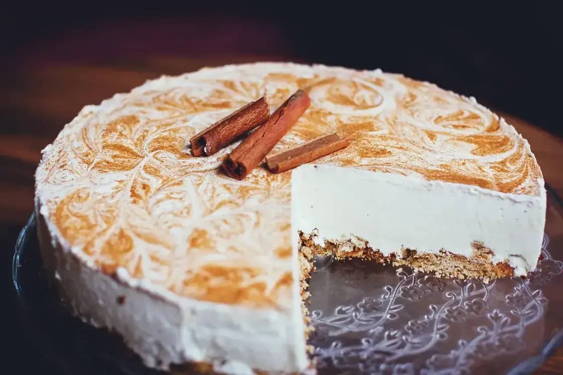 A whole cheesecake topped with cinnamon sticks, with one slice cut away