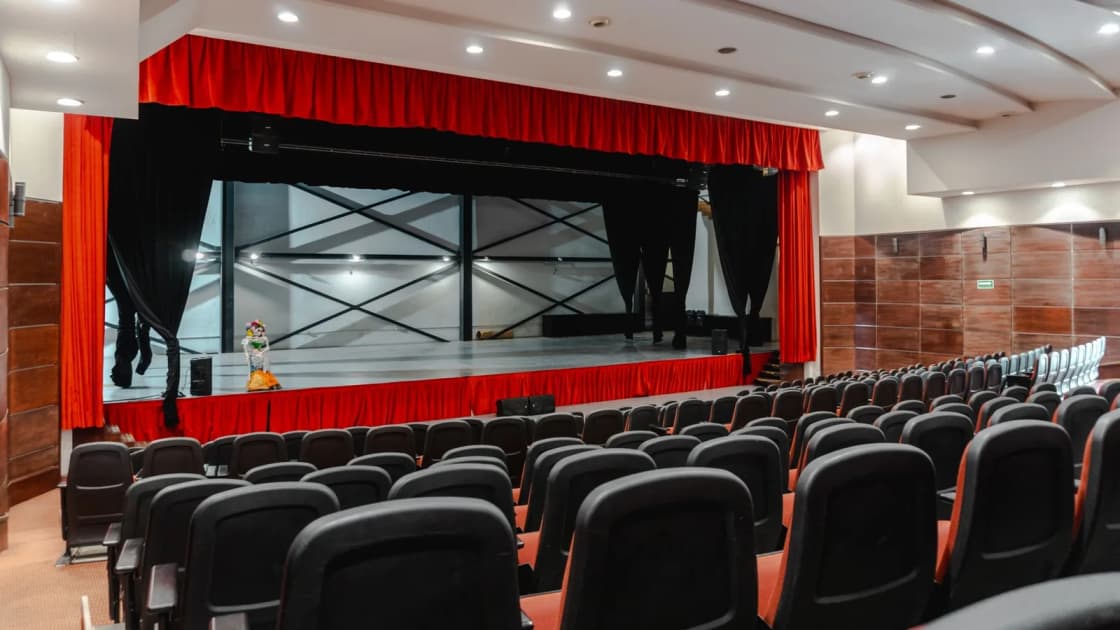 Rows of empty seats facing a stage framed by red curtains