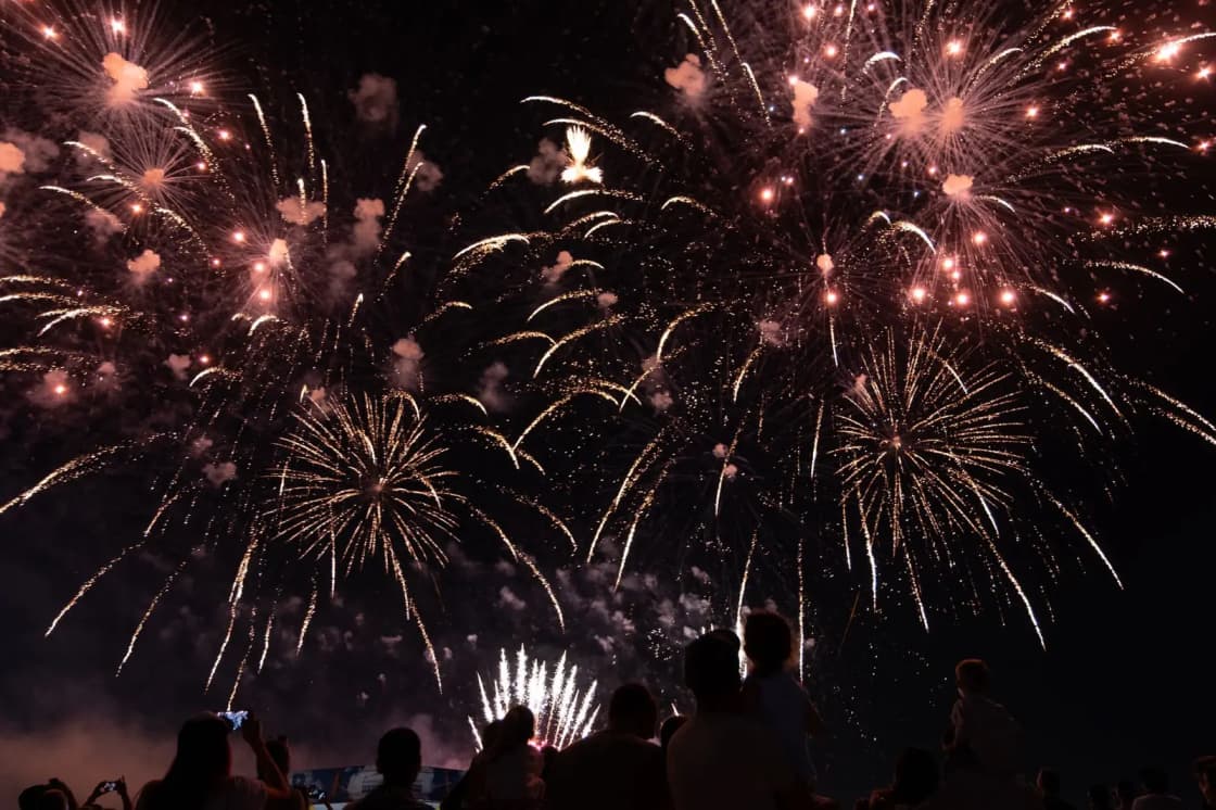 Silhouetted crowd watching a brilliant fireworks display lighting up the night sky