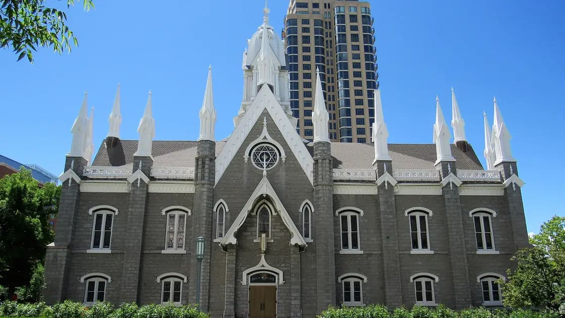 The Assembly Hall on Temple Square, a gray stone building with white spires, with a modern tower rising behind it