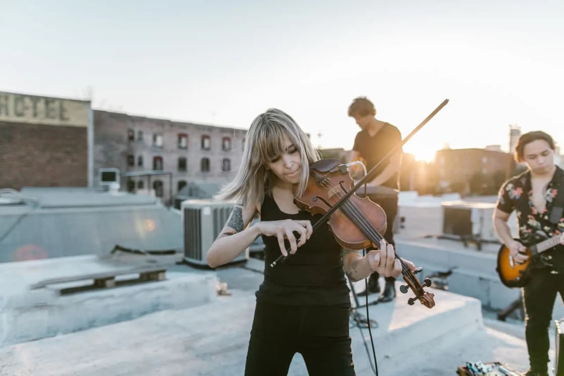 Woman violinist performing with a band on a rooftop during sunset, creating a warm and lively atmosphere
