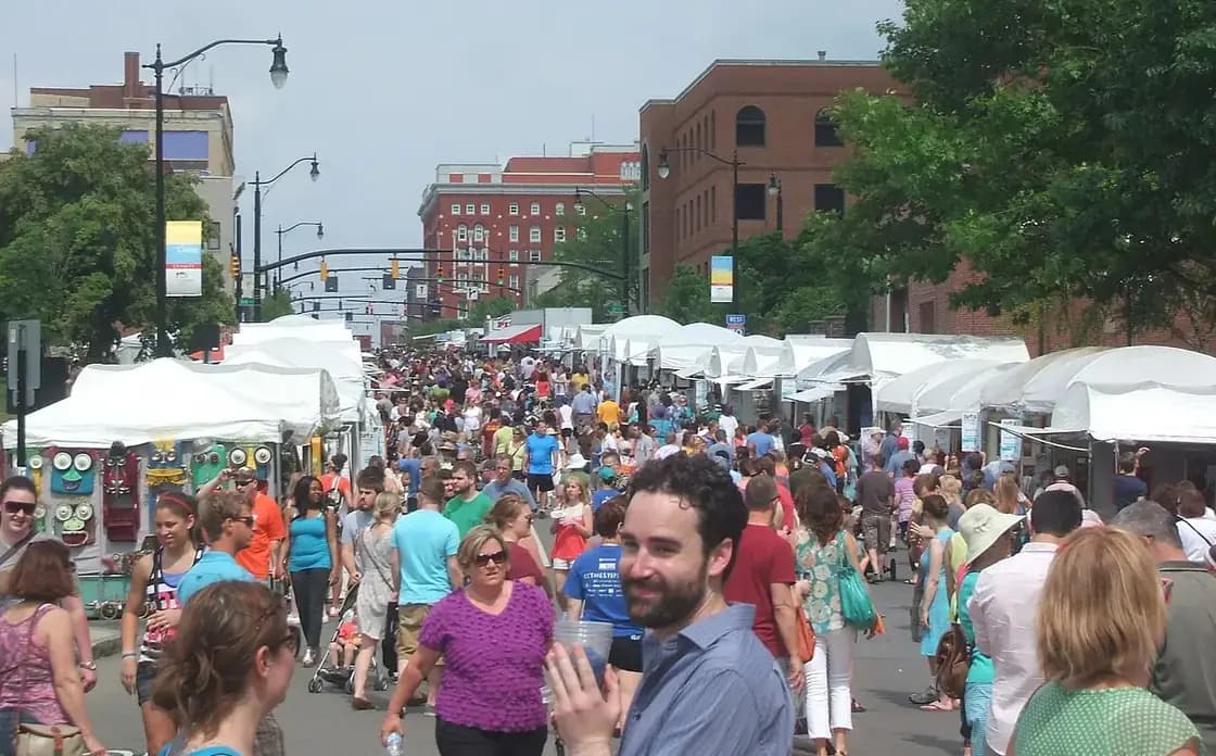 Craft festival booths and crowds on a small-town main street with mountains behind