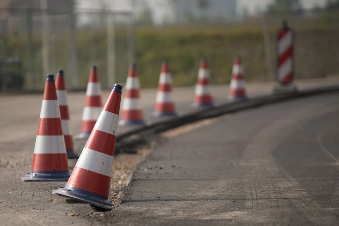 A row of orange and white traffic cones along the edge of a newly paved road