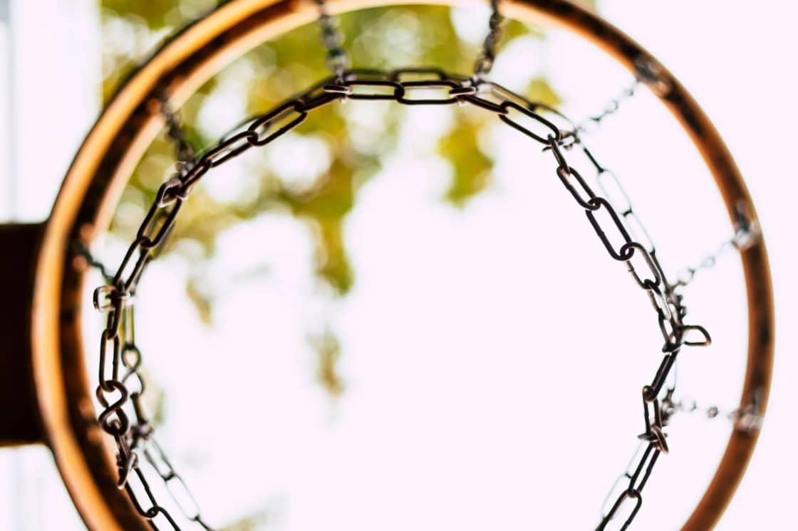 Looking up through a chain-net basketball hoop at a bright sky and blurred leaves