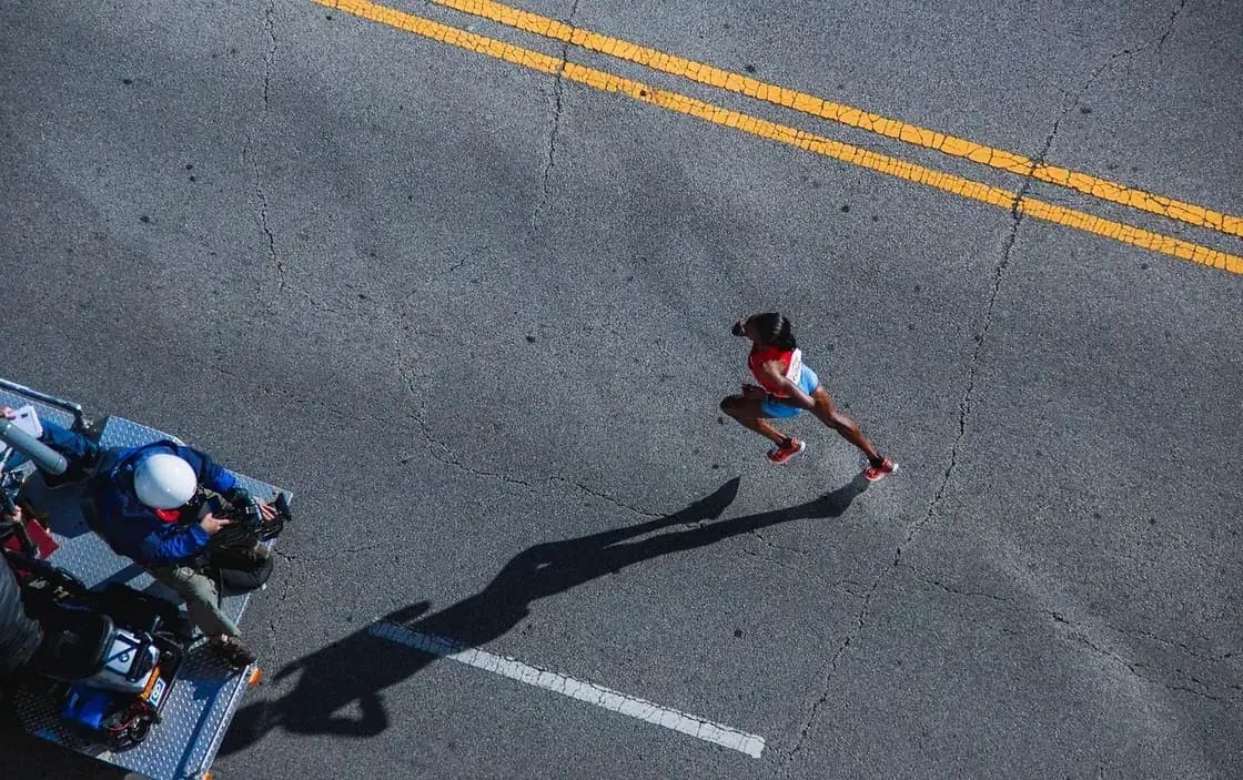 A runner on an empty road seen from above, photographers at the roadside