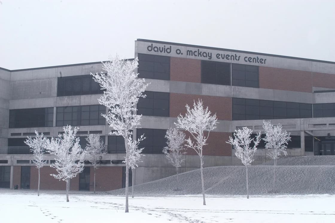 The David O. McKay Events Center at Utah Valley University in Orem, Utah, its brick and concrete facade behind a row of frost-covered young trees on a snowy winter day