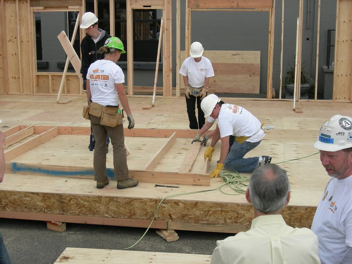 Volunteers in hard hats and tool belts framing the floor of a house on an organized build day