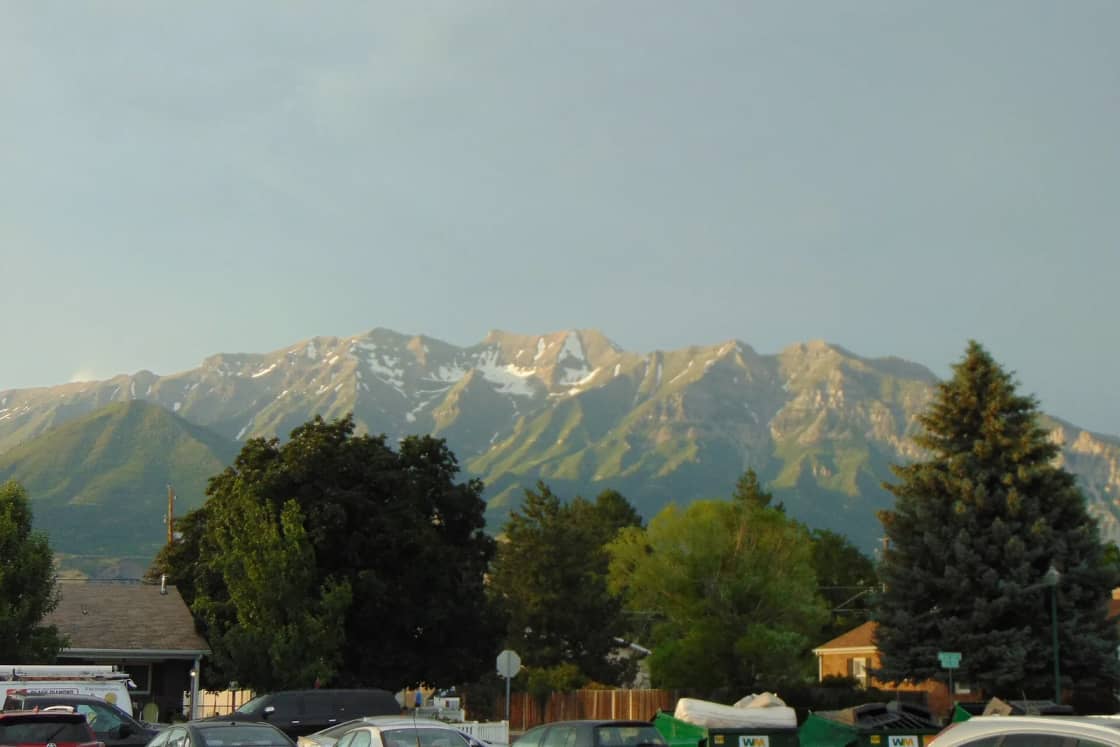 Mount Timpanogos with late snow rising above trees, rooftops and parked cars in Orem, Utah.