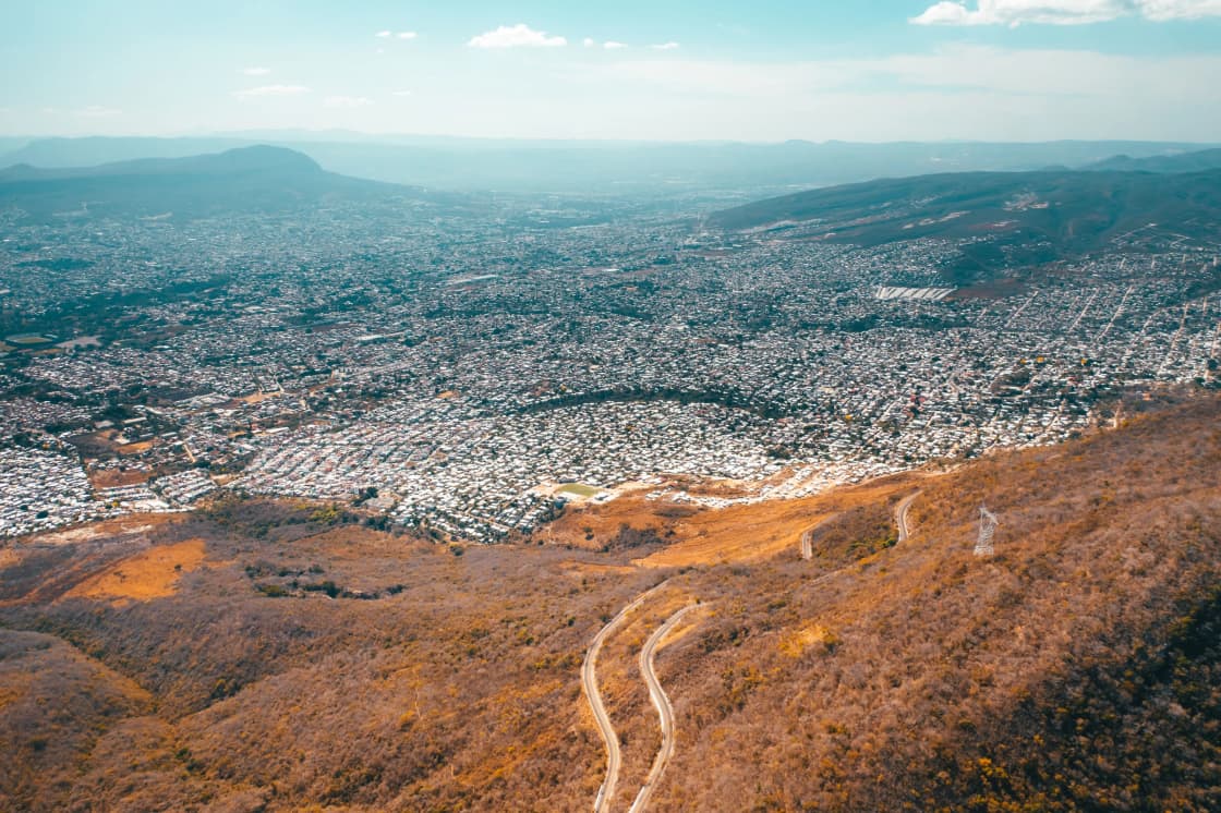 An aerial view of a large city spreading across a valley floor below dry foothills