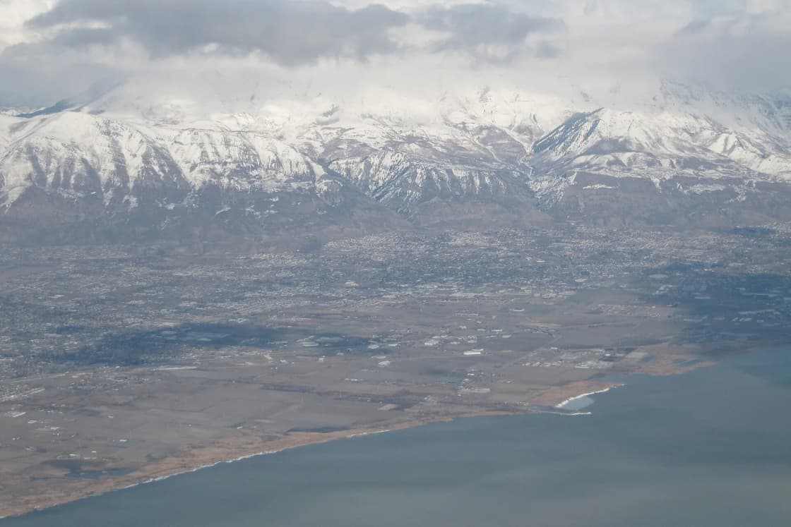 Aerial view of northern Utah Valley towns between the Utah Lake shore and the snow-covered Wasatch Range.