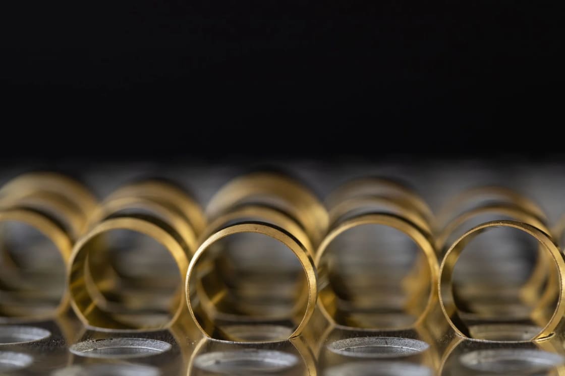 A row of plain gold rings standing on end on a dark reflective surface
