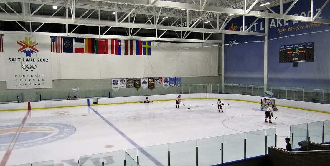 Skaters on the ice at Peaks Ice Arena in Provo, beneath a Salt Lake 2002 banner and a row of national flags