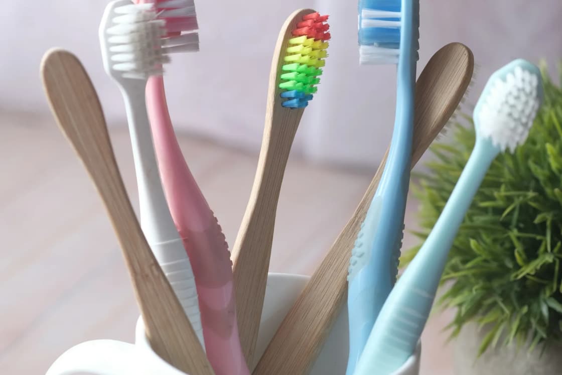 A white mug holds a family's toothbrushes, including small children's brushes with bamboo handles and soft colored bristles.