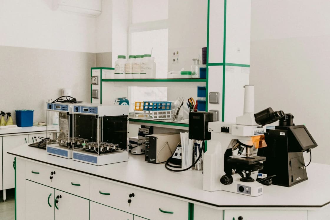 A bright, empty research lab with a microscope, analytical instruments and reagent bottles lined up along a white workbench.