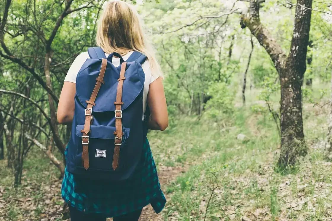 A woman with a backpack walking a wooded trail