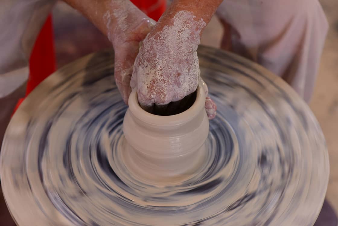 Hands shaping a tall clay form on a spinning pottery wheel