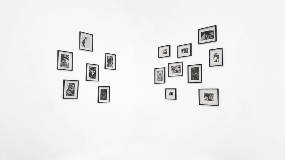 Two clusters of small black-framed photographs hung on a plain white gallery wall