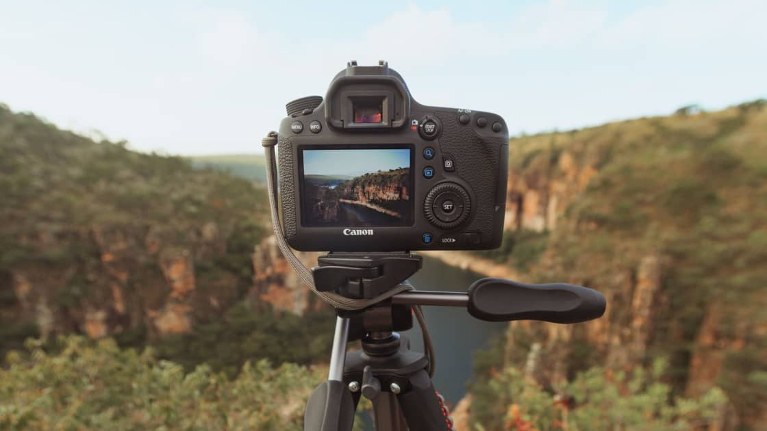 A DSLR camera on a tripod framing a steep canyon, with the scene visible on the camera's rear screen and the drop softly out of focus behind it