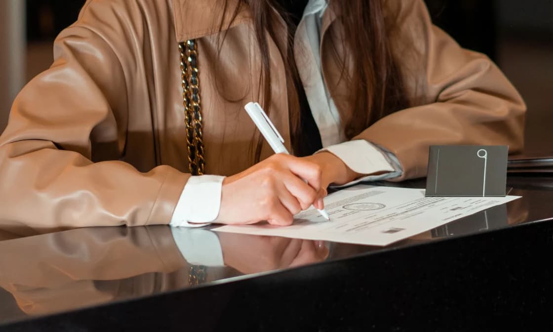 A person signing a printed form at a dark polished service counter