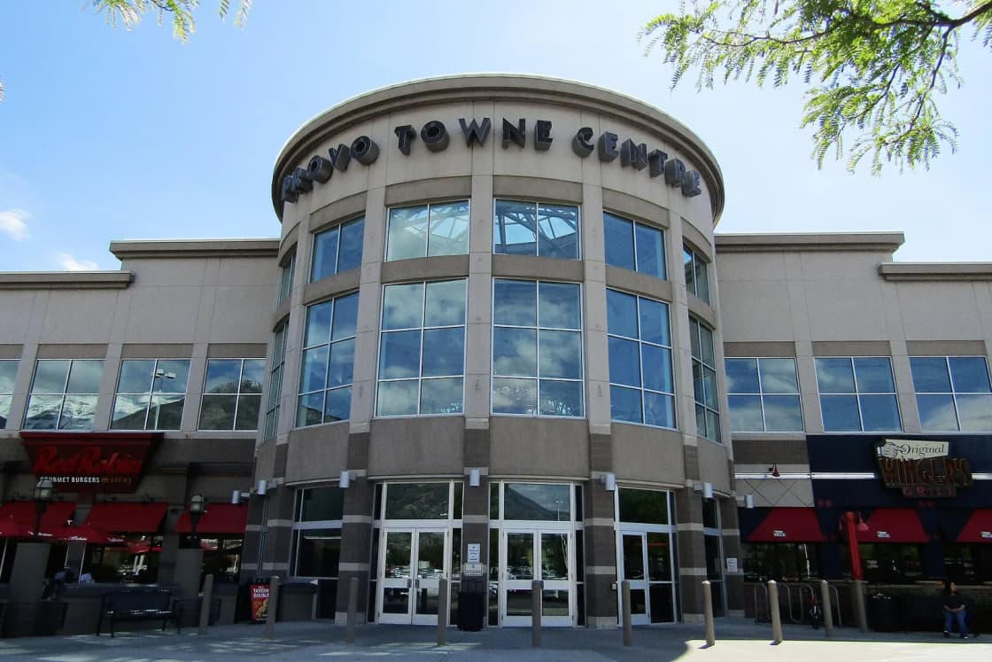 The rounded glass entrance of Provo Towne Centre under a blue summer sky, the mall's name in tall letters across the top and restaurant awnings on either side