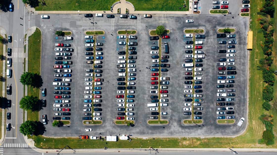 A straight-down aerial view of a parking lot packed to capacity, six long rows of cars filling every stall between grass verges