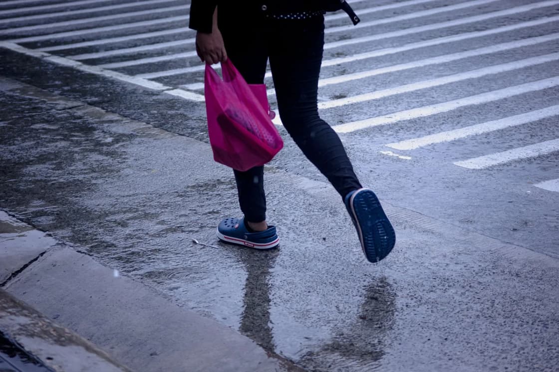 A person crossing a wet street on foot carrying a shopping bag