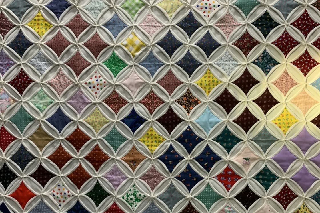 Close-up of a pieced quilt in a cathedral-window pattern, small squares of colored prints framed by curved white fabric.