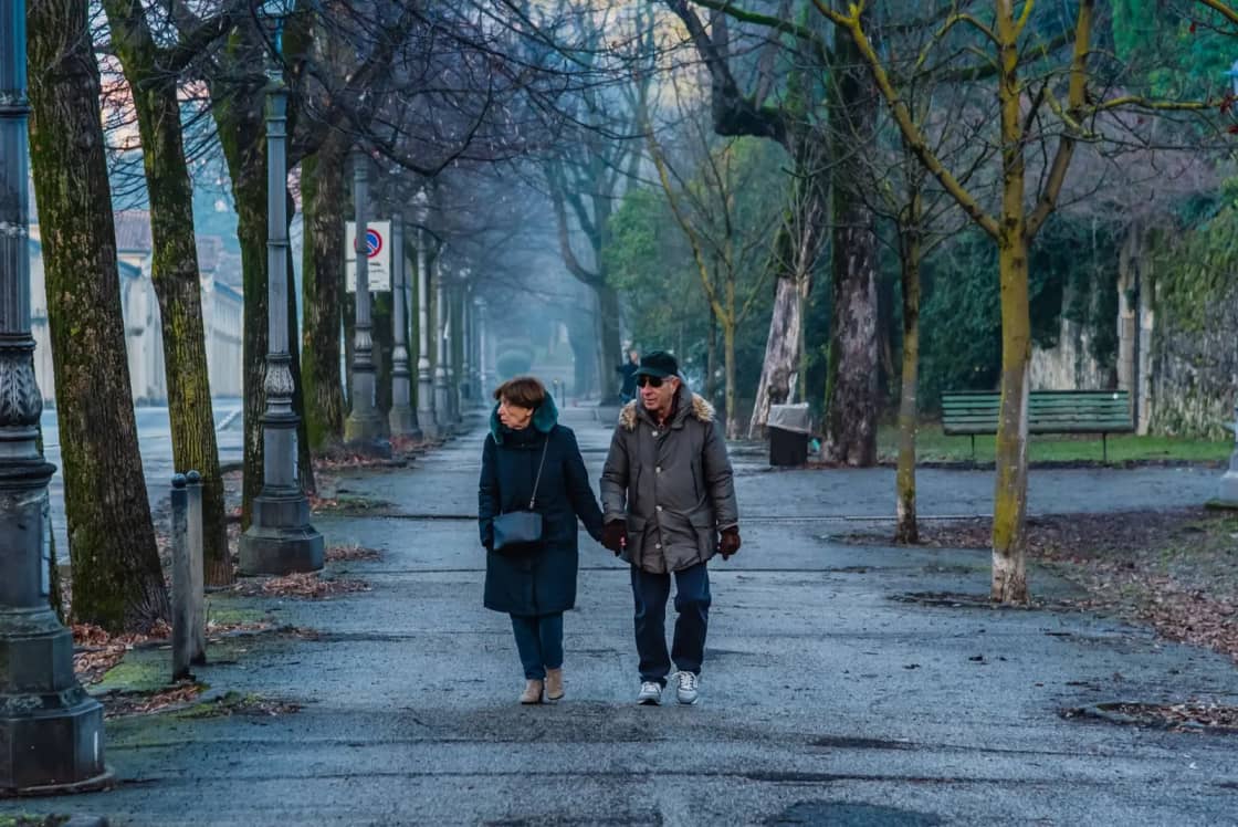 An older couple walking hand in hand along a park path