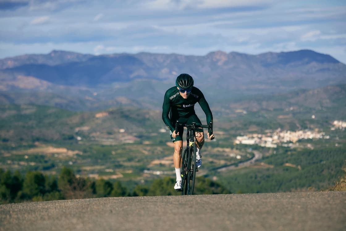A cyclist climbing a road with a wide hazy mountain valley spread out behind