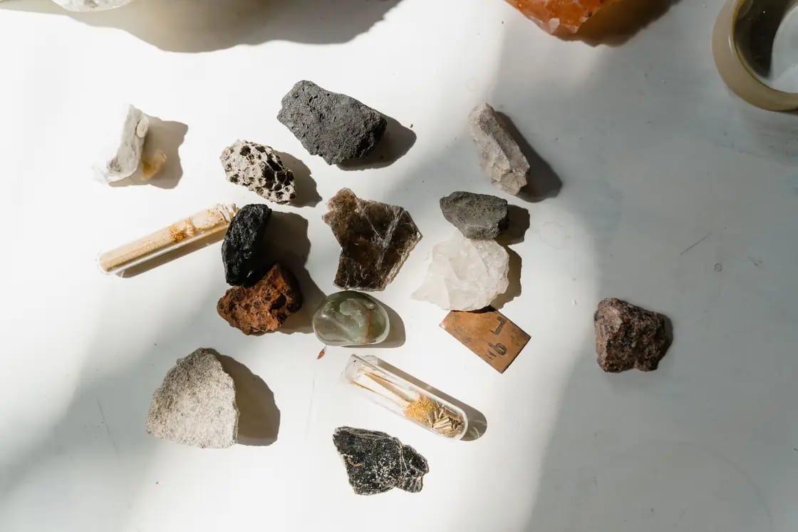 A spread of small collected rock and mineral specimens on a white surface, including a clear crystal point and porous volcanic fragments