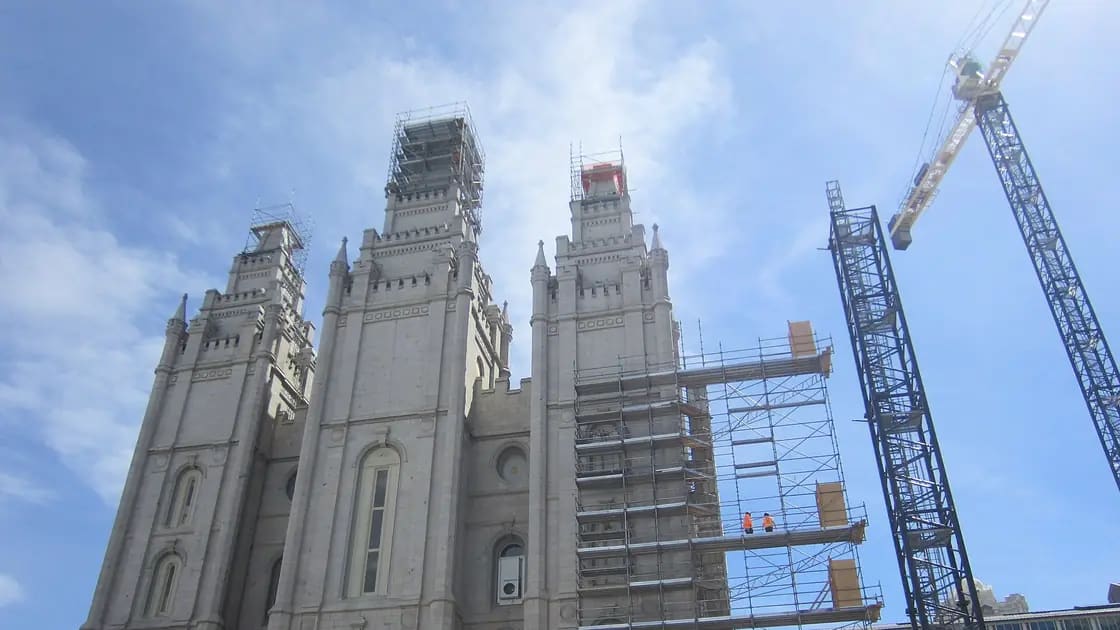 The Salt Lake Temple's granite spires wrapped in scaffolding, with two construction cranes beside it, during its renovation