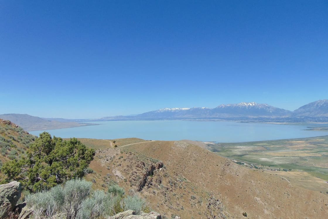 Utah Lake seen from dry juniper hills to the south, with snowcapped Wasatch peaks across the water.