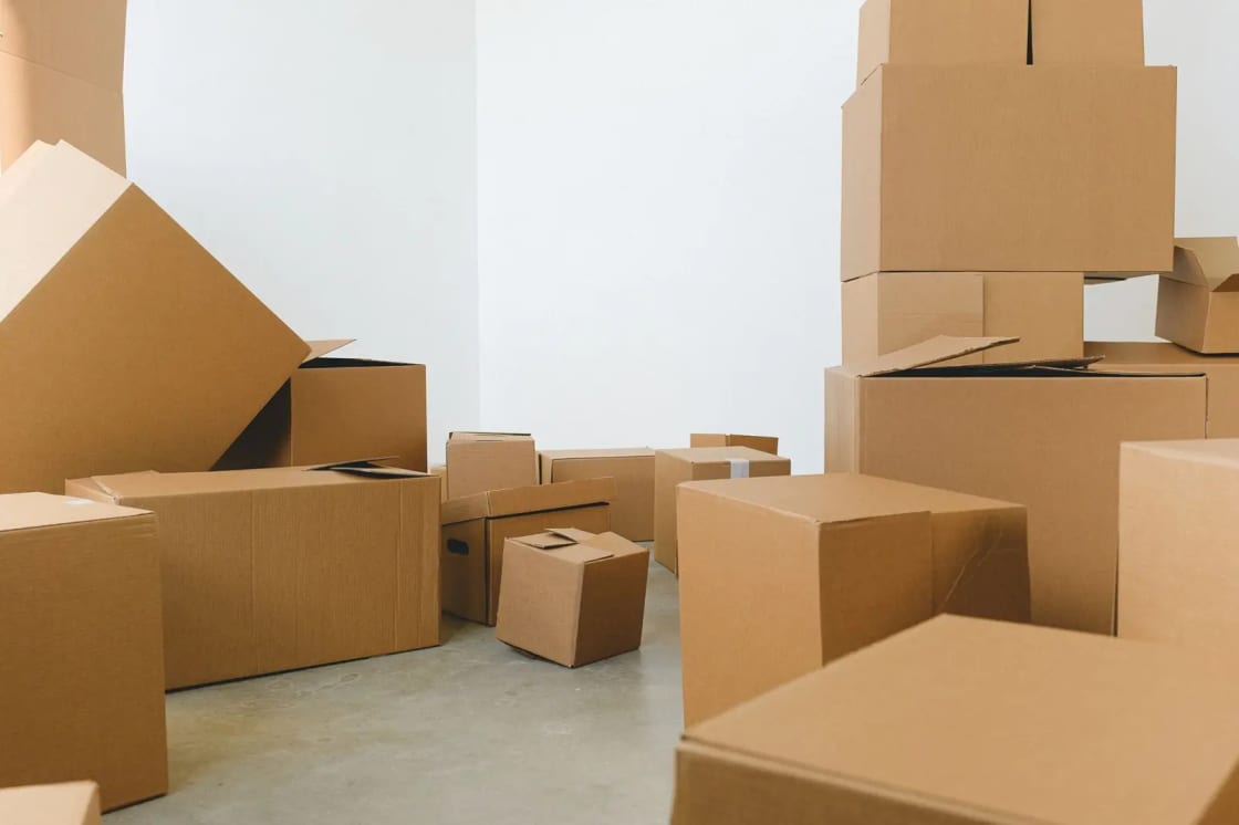 Stacked cardboard moving boxes of several sizes in an otherwise empty room with white walls