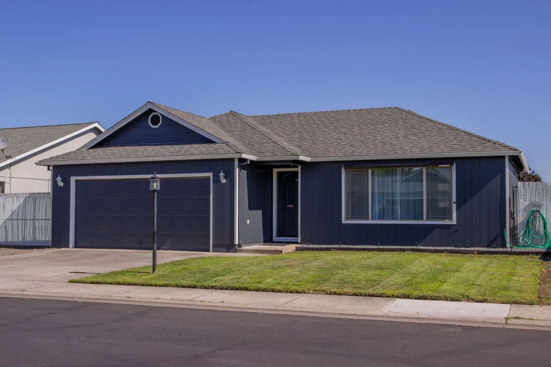 A single-story ranch house with dark blue siding, an attached two-car garage and a freshly mowed front lawn, on a quiet street under a clear sky