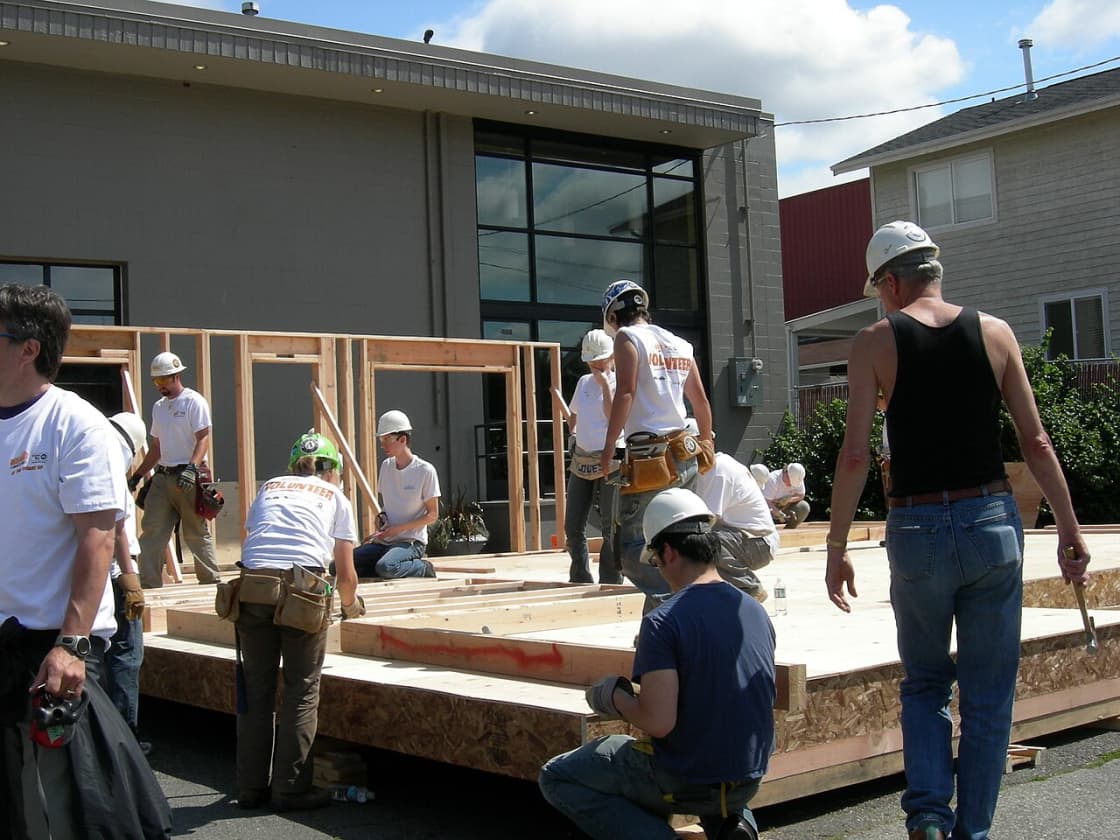 Volunteers in hard hats assembling a timber wall frame at a Habitat for Humanity build