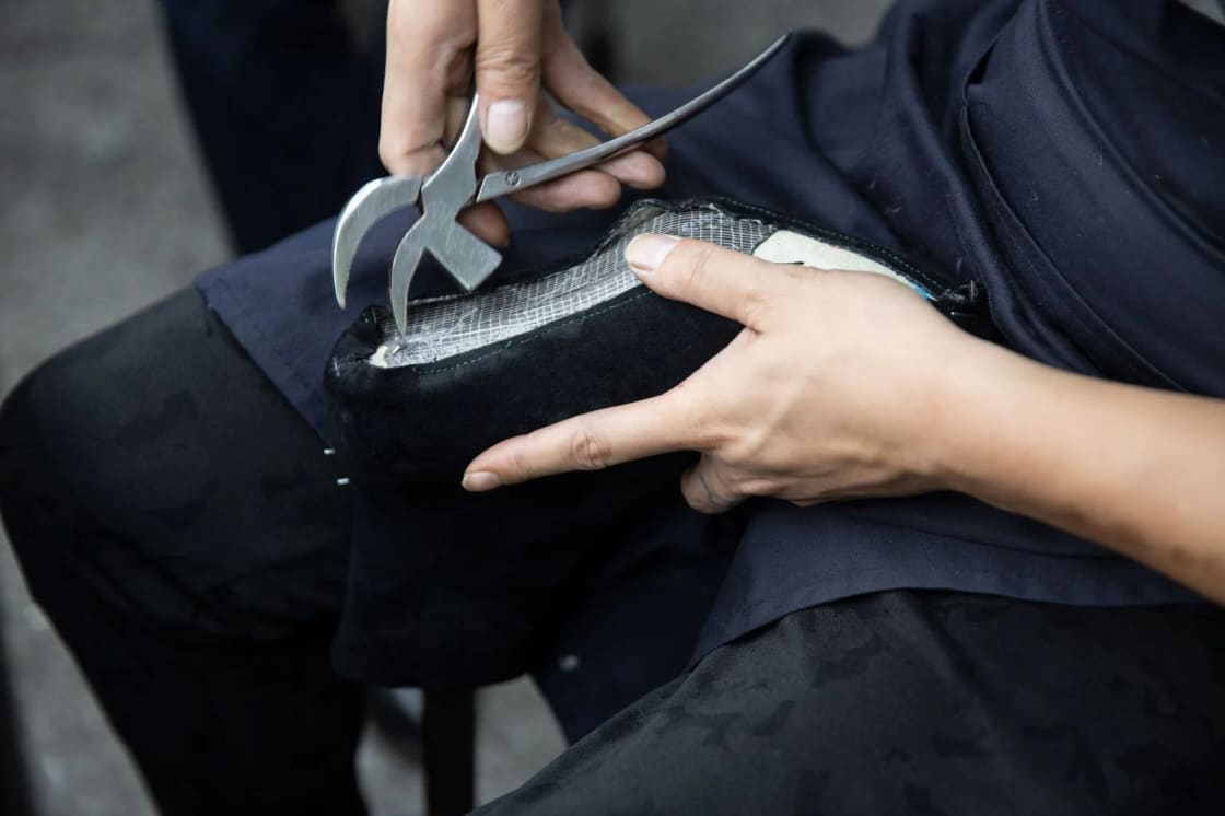 Hands using lasting pincers to pull the upper of a black shoe back over its insole