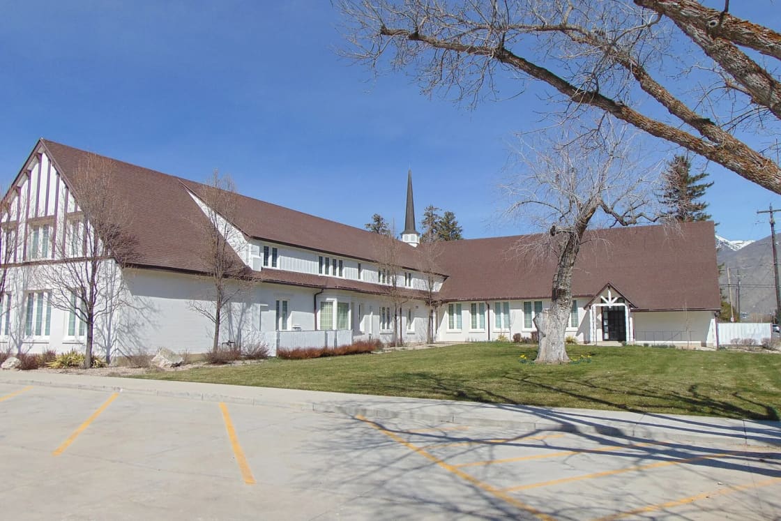Mapleton's white church with dark timber trim and a tall steeple, set behind a parking lot and leafless trees on a spring day