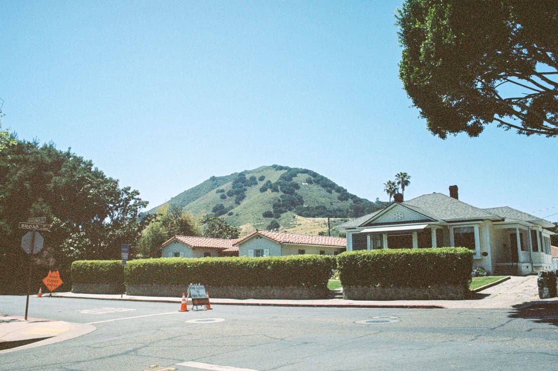 Single-story houses along a residential street with a green hill rising behind
