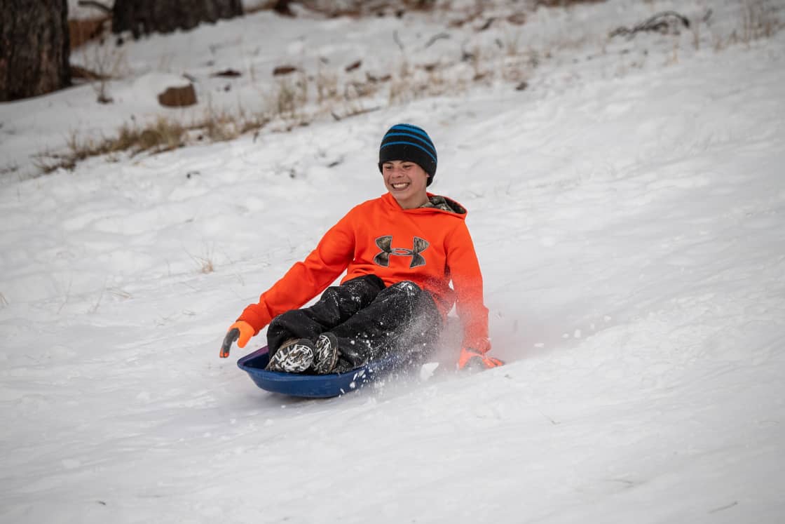 A child riding a plastic sled down a snowy slope, dragging one gloved hand in the snow