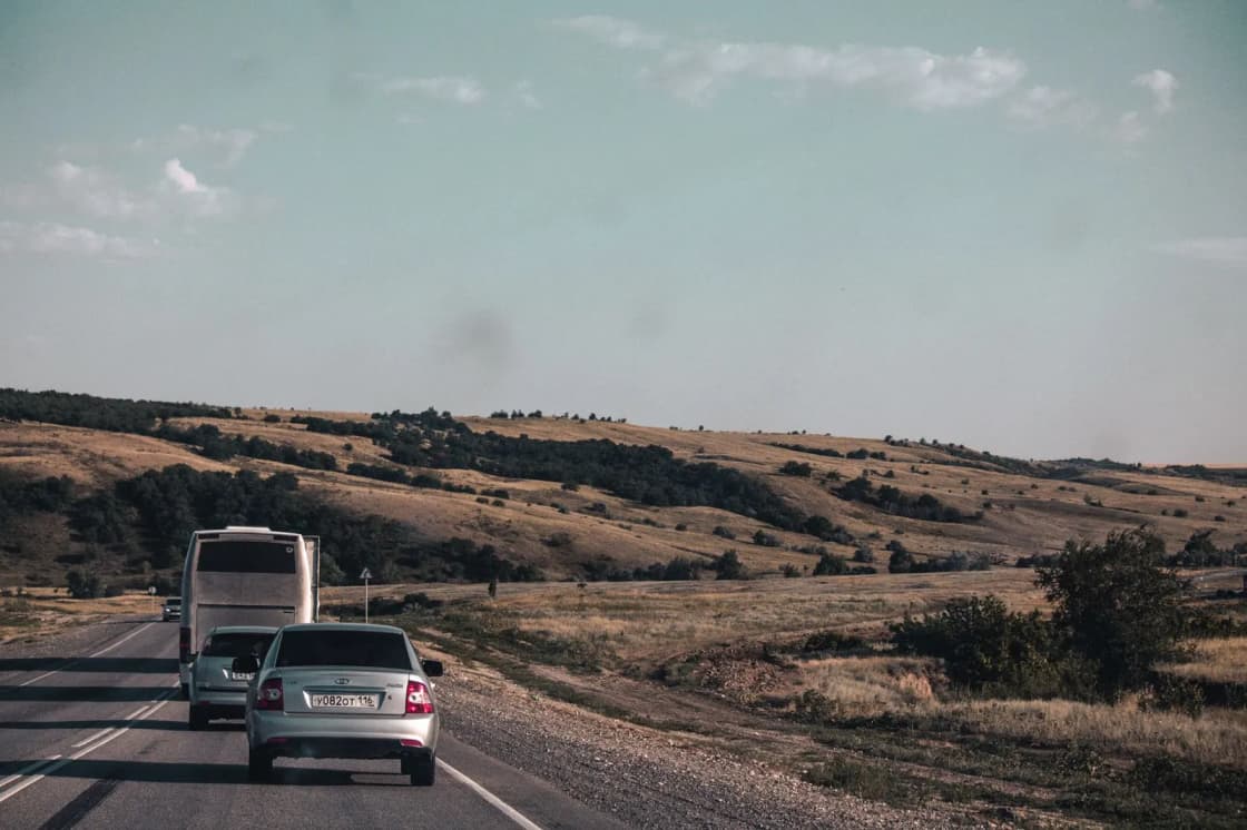 A car following a box truck along a two-lane highway through dry rolling grassland under a pale sky