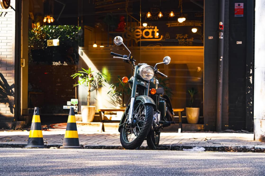 A vintage motorbike stands beside a cozy cafe on a sunny urban street