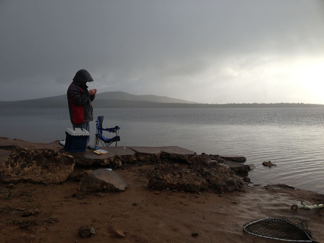 A person standing on the rocky shore of Strawberry Reservoir in low mist, with flat water stretching to the far bank