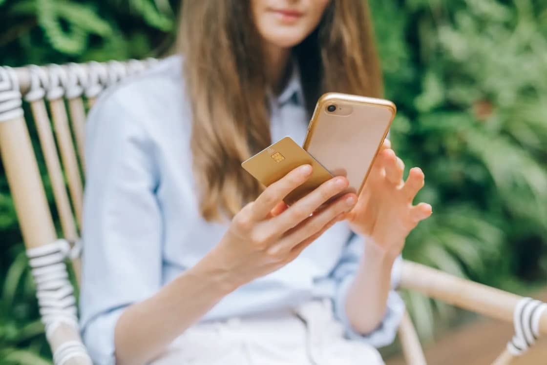 A woman making an online purchase using a smartphone and credit card outdoors