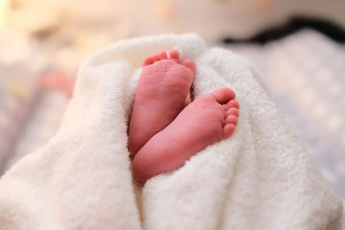 A newborn's tiny bare feet peeking out of a soft white blanket